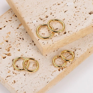 Three pairs of gold minimalist round hoop earrings on natural beige stone blocks