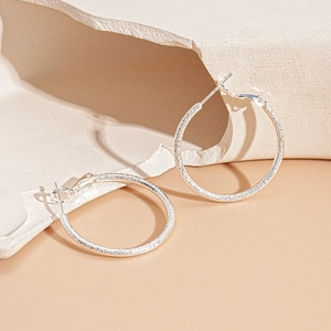Detail view of silver geometric hoop earrings with a textured frosted finish on a prop