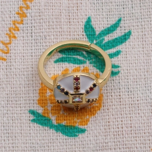 Vue détaillée d'une bague dorée sertie de zircons colorés et émail blanc élégant