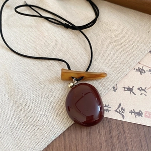 Detail of vintage round resin pendant with dark brown luster and elegant t-bar clasp