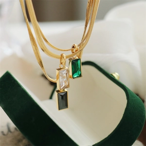 Close-up of emerald and diamond rectangle pendants on gold snake chains in a velvet box