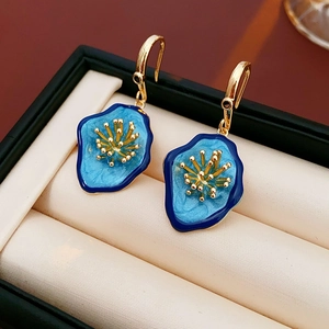 Close-up of vintage flower earrings with blue enamel and gold hooks in a jewelry box