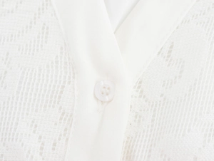 Nahaufnahme der weißen Spitzentextur und Knopfdetails an einem eleganten Kleid