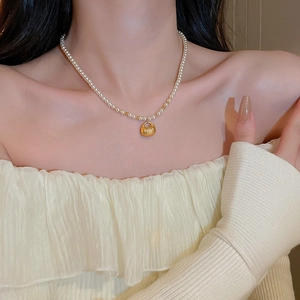 Detail of a pearl necklace featuring a golden lucky pouch pendant on a female neck