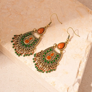 Detailed macro view of bohemian retro earrings with orange resin and green bead tassels