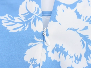Nahaufnahme des weißen Reißverschlusses an einem blau geblümten Kleid mit Blattmuster