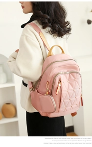 Mochila rosa de nailon oxford con tachuelas y colgante a juego en un entorno suave