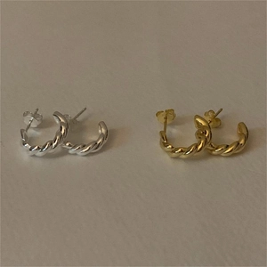 Detail of twisted metal hoop earrings in gold and silver finish on a plain surface