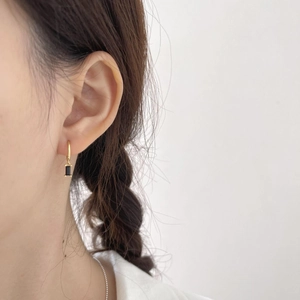 Detail of gold huggie hoop earring with rectangular black zircon stone on model