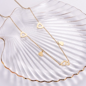 Minimalist gold titanium steel necklace with heart pendants in a glass shell dish