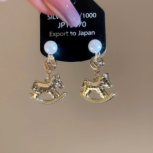 Macro shot of gold rocking horse earrings with pearl accents and hammered texture