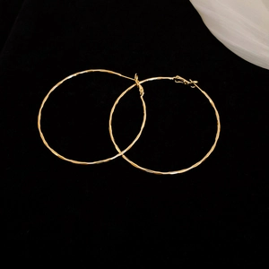 Detail view of large gold hoop earrings with hammered texture on black velvet