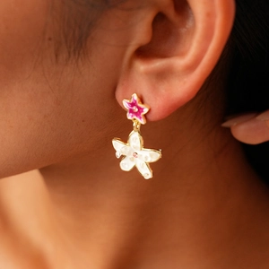 Close-up of elegant star and flower earrings with pink and white enamel details