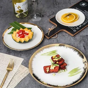 Nordic ceramic dinner plates with gold rim and artistic feather design on a dark table