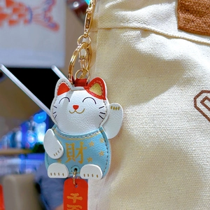 Cute Maneki-neko leather keychain accessory on white canvas bag with gold metal hardware