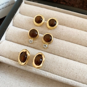 Macro shot of three vintage tiger eye geometric stud earrings on beige velvet tray