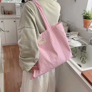 Close-up of pink and white striped canvas tote bag with woven label in lifestyle setting