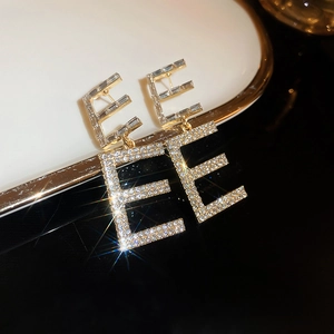 Macro shot of gold E-shaped letter earrings with shimmering baguette and round zircons