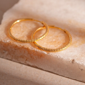 Detailed close-up of golden hoop earrings featuring a vintage hammered textured surface