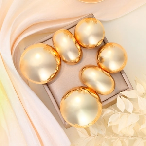 Detail of glossy gold geometric earrings on beige display mat with silk background