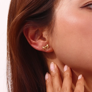 Close-up of a woman wearing a mini gold bow stud earring with 18K gold plated finish