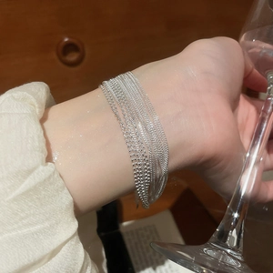 Close-up of elegant multi-layer silver bracelets worn with a glass in a lifestyle setting