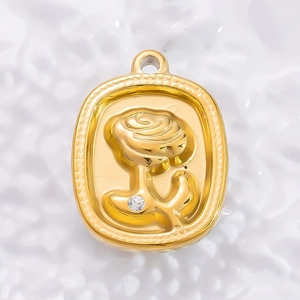 Macro detail of 18K gold plated oval pendant with embossed rose and single rhinestone