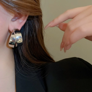 Close-up of oversized polished silver hoop earrings with a double cross circular design