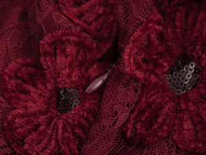 Macro view of dark red lace fabric with floral jacquard texture and black sequins detail