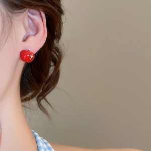 Detail view of a model wearing asymmetrical red apple stud earrings with a glossy finish