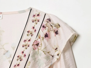 Detail of pink floral top with V-neck, black piping, and ruffled shoulder design
