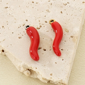 Detail of red chili pendants with gold and silver clasps on a textured stone base