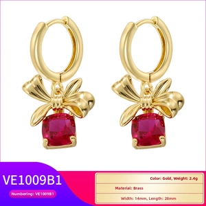 Detail of gold brass earrings with a ribbon bow and square red crystal pendants