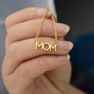 Close-up of a gold Mom pendant necklace held in hand showing detailed letter design