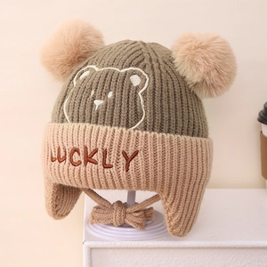 Detail of army green knit trapper hat featuring dual yellow pom-poms and bear embroidery