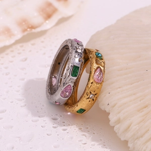 Close-up of gold and silver rings with pink drop and green rectangle zircons on shells