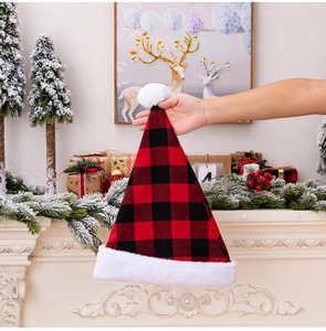 Detail of red and black plaid Christmas hat with white plush trim and pompom against a fireplace