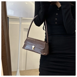 Detail of dark brown crocodile pattern texture and golden metal buckle on baguette bag