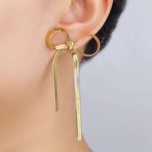 Detailed view of golden bow earrings with long snake chain tassels on a model