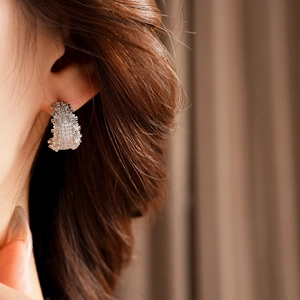 Vue macro d'une boucle d'oreille large en C argentée avec cristaux scintillants pavés