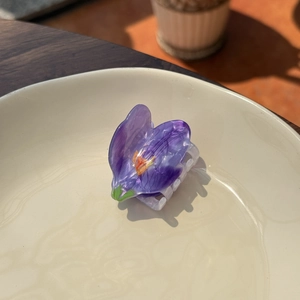 Macro detail of a purple floral acrylic hair claw clip in a white ceramic bowl