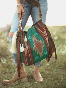 Detail view of woven bohemian shoulder bag with long brown leather tassels on grass