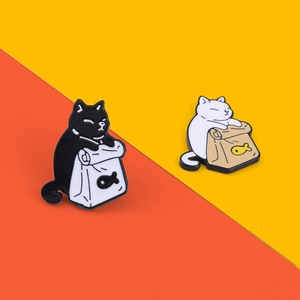 Detailed shot of black and white enamel cat pins holding fish bags on colorful background