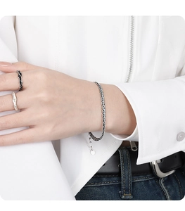 Detailed view of woven snake chain silver bracelet with round charm on wrist