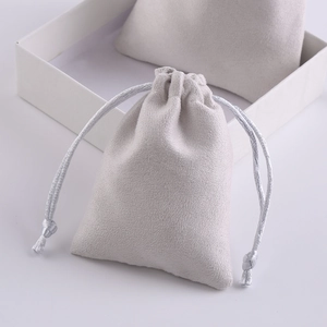 Grey microfiber suede drawstring jewelry pouch with silver braided cord on white background