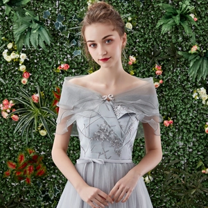 Detalle de vestido de fiesta gris con hombros descubiertos, bordado floral y capa de tul