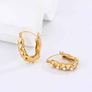 Close-up of golden U-shaped earrings with hammered texture and small pearls inlay