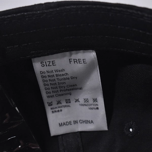 Close-up of 100% cotton fabric care label and wash instructions inside the denim baseball cap