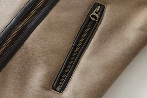 Close-up of bronze metal zippers on a brown leather jacket with visible grain texture