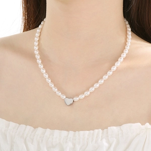 Close-up of elegant pearl necklace with a silver heart pendant on model's neckline